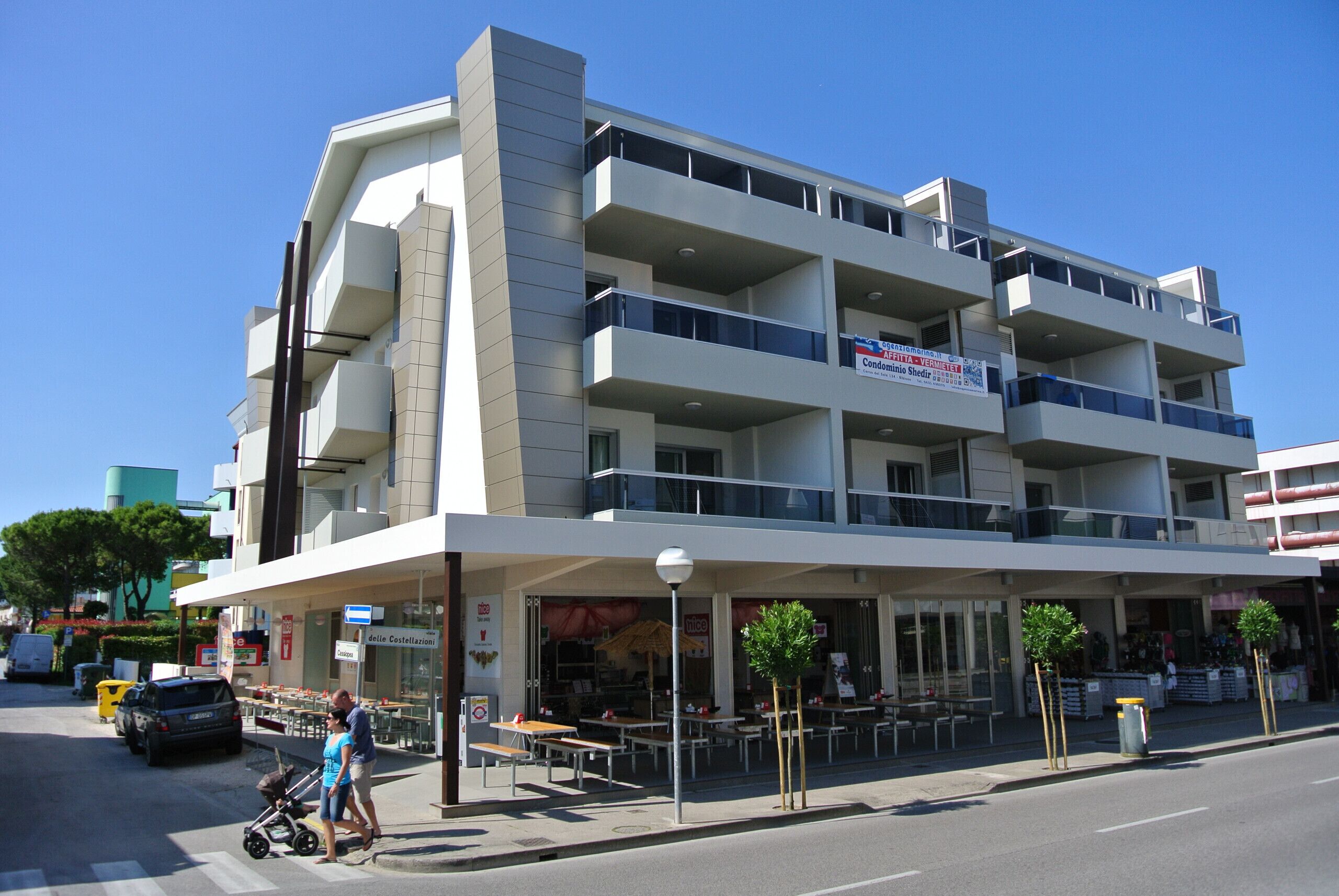 A multi-story building with balconies, a ground-level cafe, and outdoor seating.