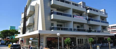 A multi-story building with balconies, a ground-level cafe, and outdoor seating.