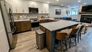 Una cocina moderna con armarios blancos, una isla grande con taburetes de bar, un horno empotrado y un televisor montado sobre la isla.