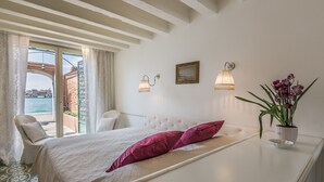 A bedroom with a bed, two wall-mounted lamps, a potted plant, and a view of the sea through a glass door. - Ca' Dell'Ulivo (Venice)