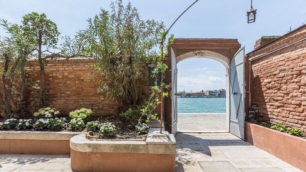 A paved pathway leading to a waterfront with a brick wall and a wooden archway. - Ca' Dell'Ulivo (Venice)
