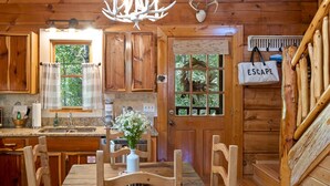 Ein rustikales Blockhaus-Interieur mit einem Holzespeisesaal, Stühlen, einer Chandelüster und einer Küchenzeile mit Fenster.