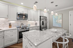 Una cocina moderna con armarios blancos, electrodomésticos de acero inoxidable, encimera de mármol e iluminación colgante.