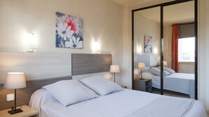 Ein modernes Hotelzimmer mit einem großen Bett, zwei Nachttischen inklusive Lampen, einem großen Spiegel und einem floralen Bild an der Wand.