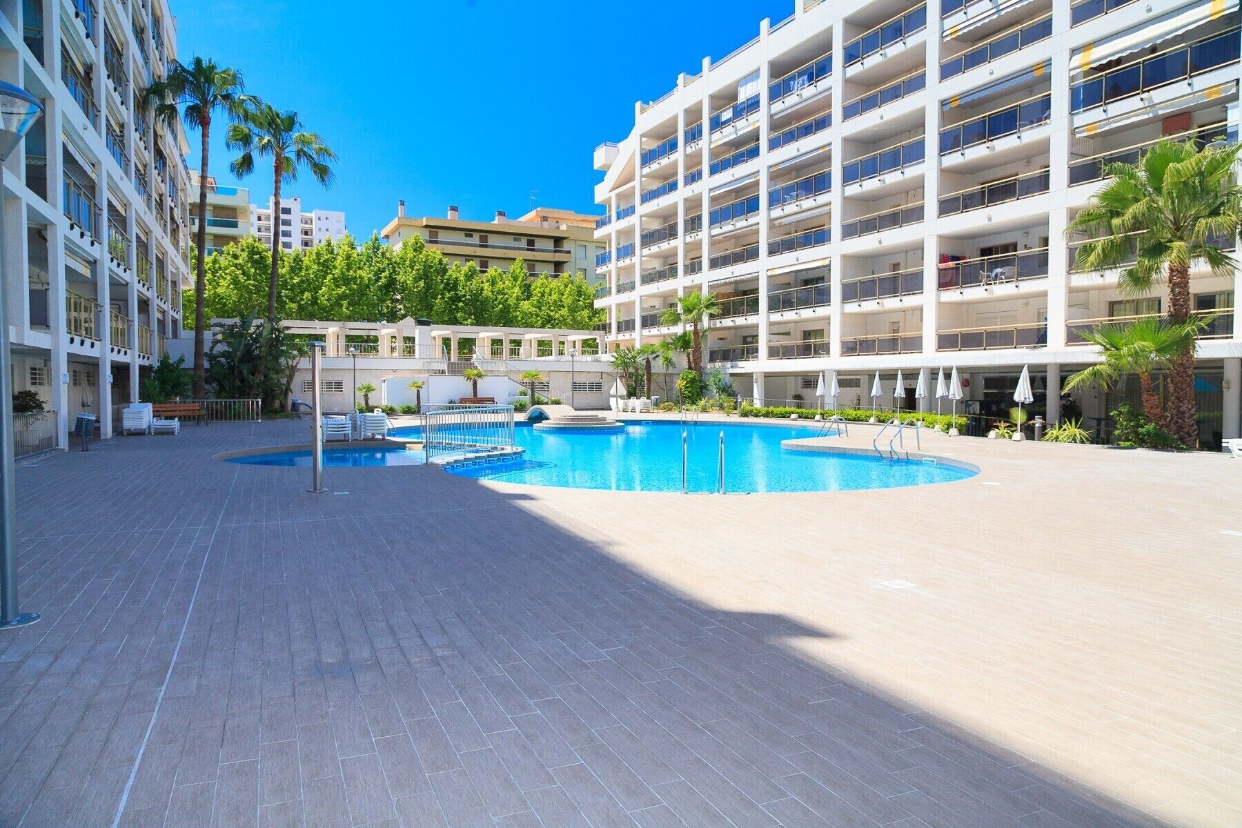 Un hôtel moderne doté d’une piscine centrale, de nombreux balcons et d’une végétation luxuriante.