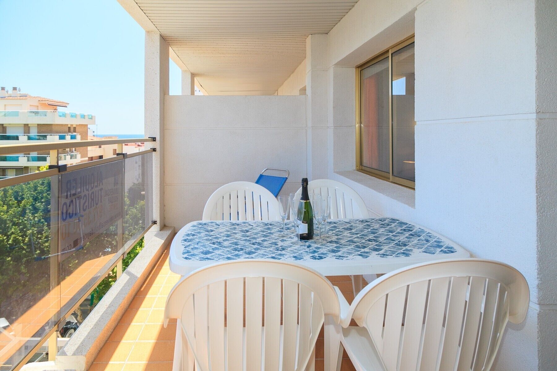 A balcony with a table and chairs, a bottle of champagne, and a view of buildings and greenery.