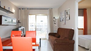 Ein Wohnzimmer mit braunem Sofa, orangefarbenen Sesseln, einem Fernseher und einem Fenster mit Vorhängen.