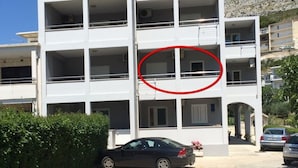 A multi-story building with a white facade, balconies, and a parking area with cars. - Apartment in Omiš with Seaview, Terrace, Air condition, WIFI (3422-2) (Omiš)