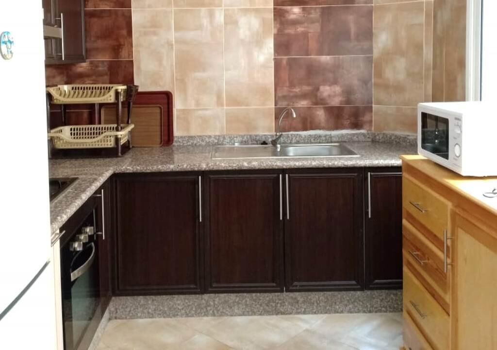 A kitchen with dark wooden cabinets, a granite countertop, a stainless steel sink, and a white microwave.