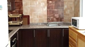 A kitchen with dark wooden cabinets, a granite countertop, a stainless steel sink, and a white microwave. - Beautiful apartment in Essaouira 4158 (Essaouira)
