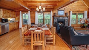 Interno di una baita in legno con un tavolo da pranzo, sedie, un caminetto e una cornice in pietra attorno al focolare, oltre a una televisione.