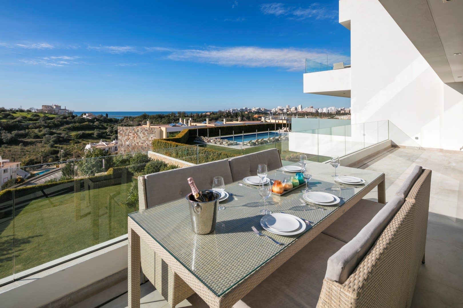 A dining area with a table set for four, overlooking a pool and a cityscape.