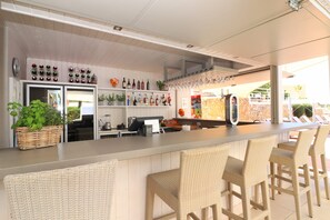 A bar area with wicker chairs, a counter, and shelves with bottles and glasses.