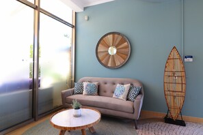 A room with a sofa, a round wall decoration, a surfboard, and a small table with a plant.
