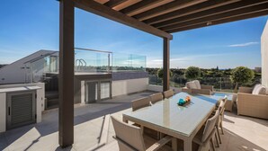 Una terraza en la azotea con barandilla de cristal, mobiliario exterior y vistas del paisaje.