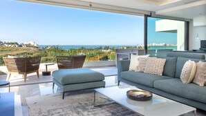 Een moderne woonkamer met een grote glazen deur die uitkomt op een balkon met uitzicht op de kust.
