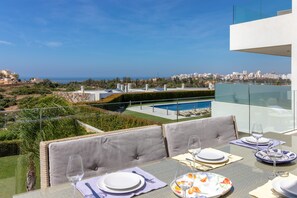 A dining area with a table set for two, overlooking a swimming pool and a cityscape.