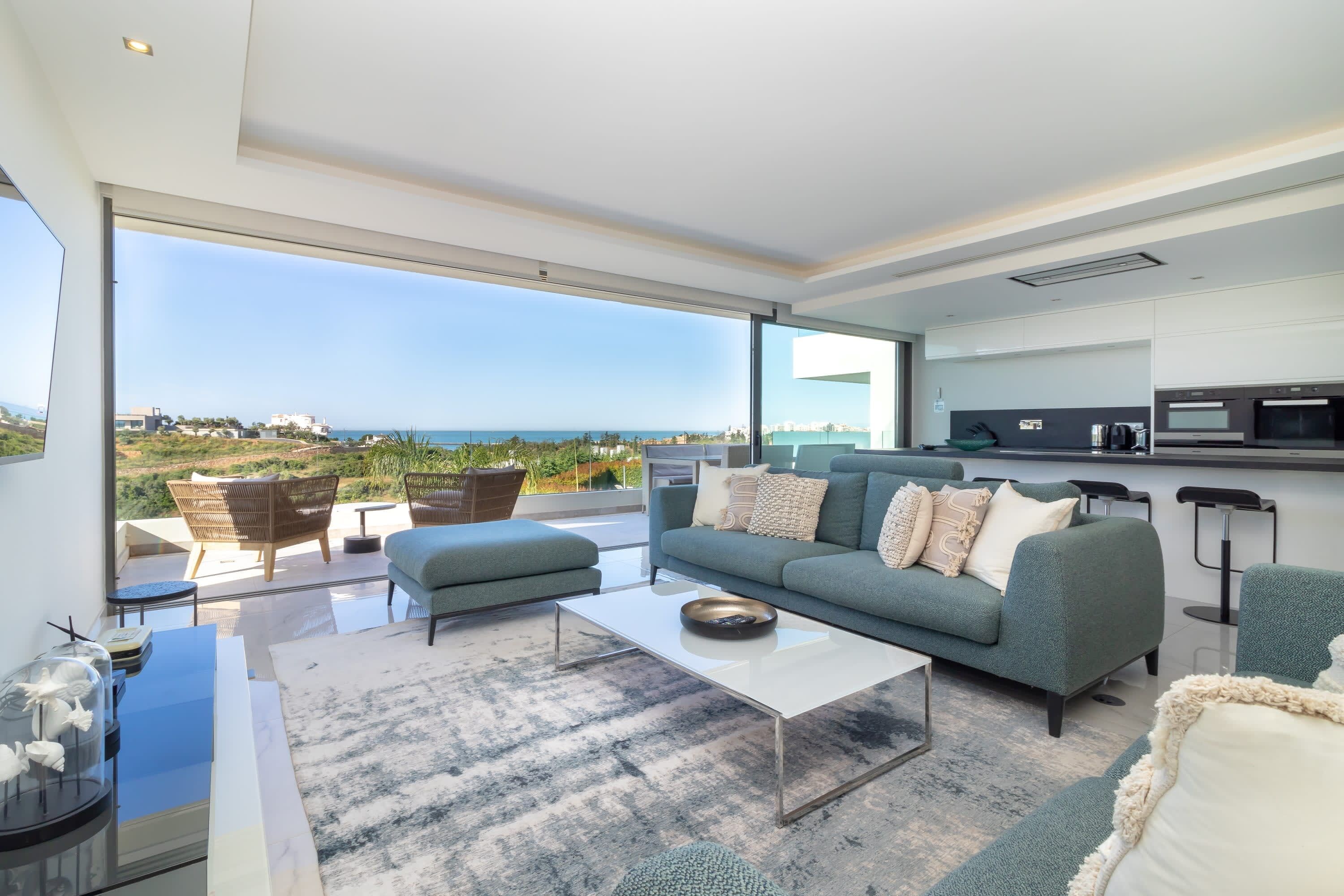 A modern living room with a large sofa, a coffee table, and a view of the sea.