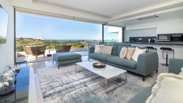 Una sala de estar moderna con un sofá grande, una mesa de centro y vista al mar.