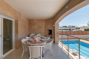 A balcony with a dining table and chairs, a pool, and a view of the city.