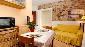 A cozy dining area with a table set for two, a red vase with flowers, a stone wall, and a yellow sofa. - Vacation Home in Capannori with 1 bedrooms sleeps 2 (Capannori)