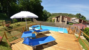 A wooden deck with a pool, blue lounge chairs, and a white umbrella. - Vacation Home in Capannori with 1 bedrooms sleeps 2 (Capannori)