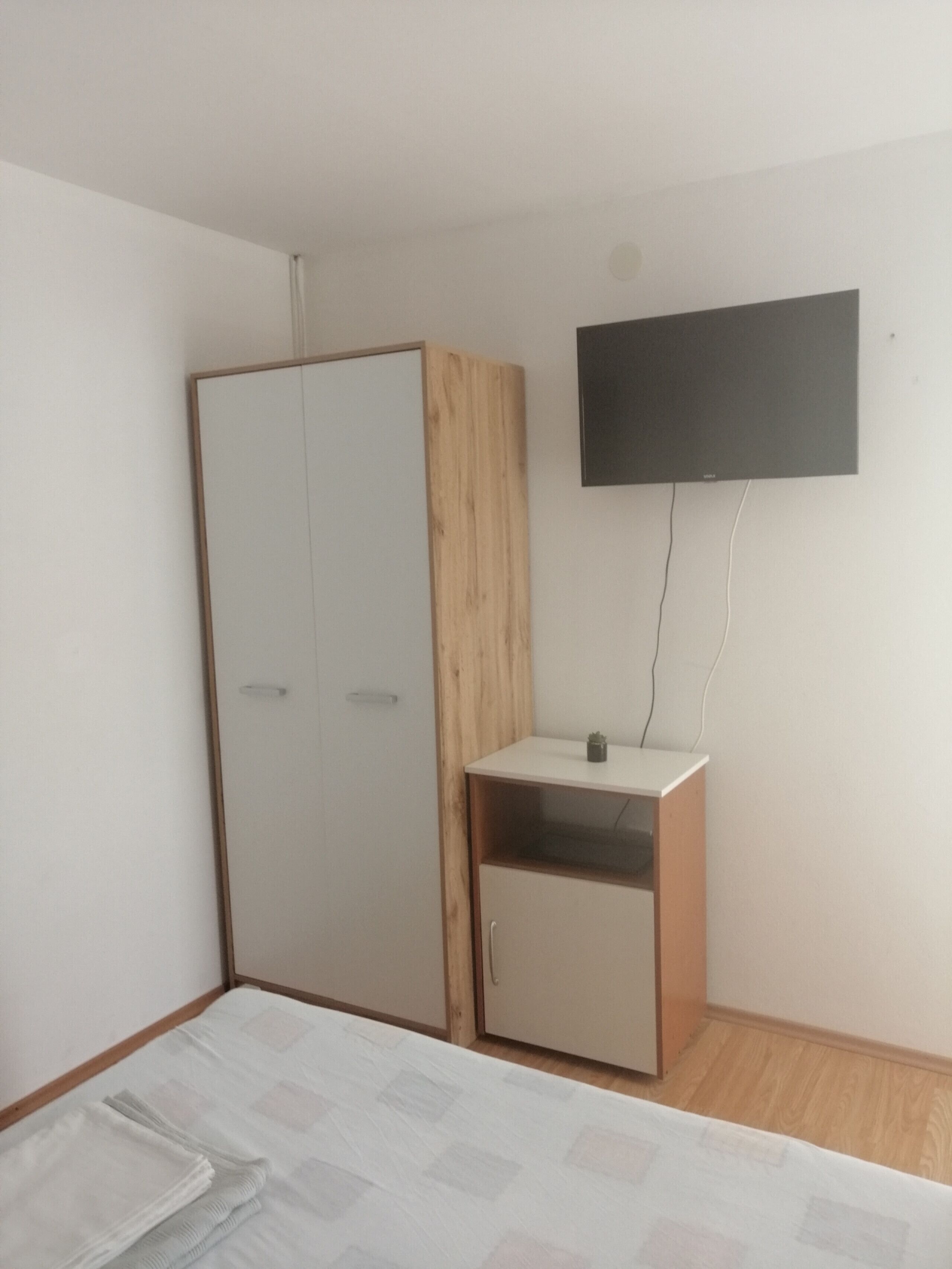 Une chambre à coucher comprenant un lit, une armoire, un petit bureau et un téléviseur fixé au mur.