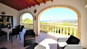 A covered patio with a table and chairs, two arches with a view of the city, and a balcony railing. - Impala - Javea, Costa Blanca (Javea)