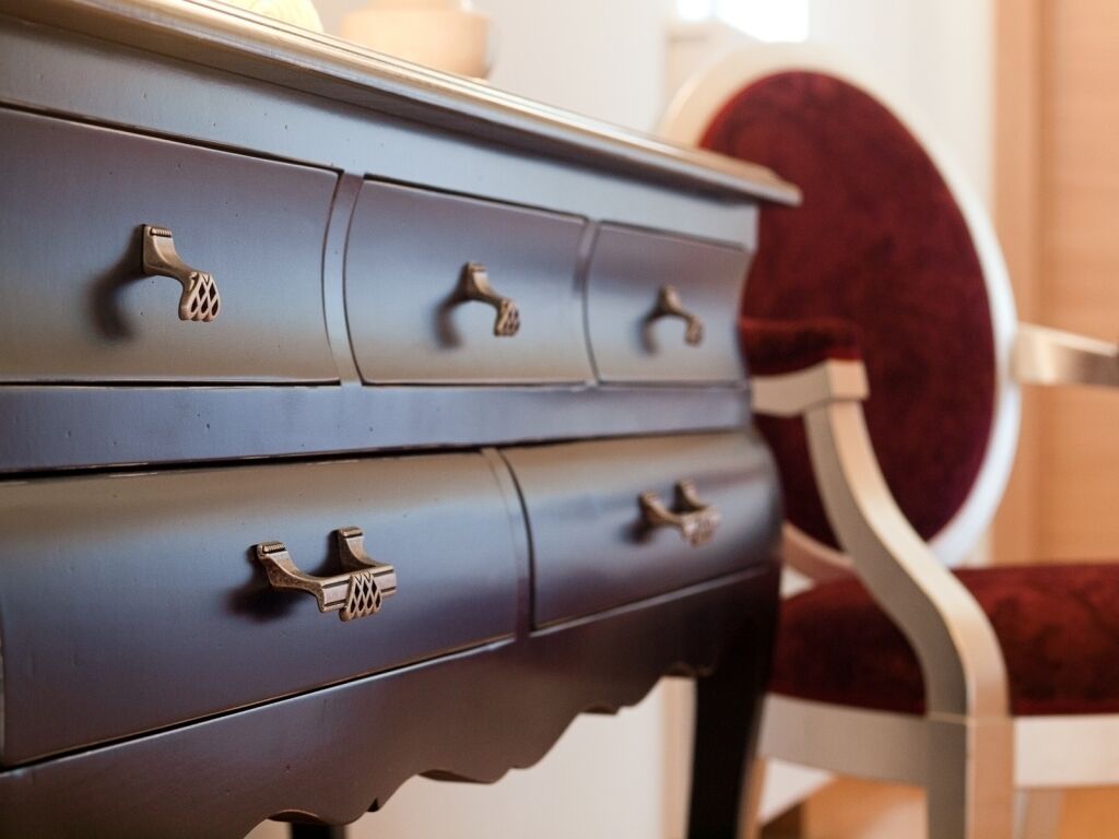 A blue dresser with ornate handles and a red chair in the background.