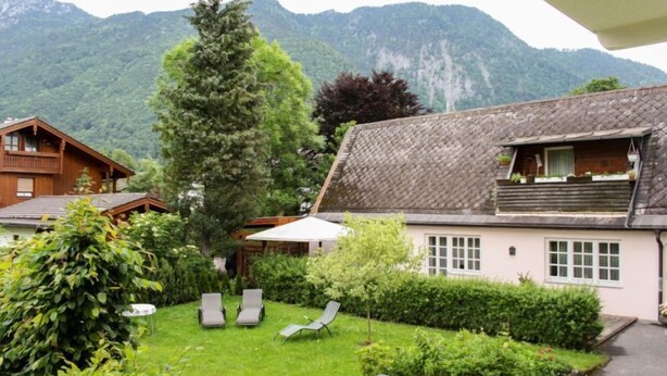 Ein gemütliches Chalet mit einem geneigten Dach, einem hölzernen Balkon und einem gepflegten Garten mit Rasen und Sträuchern.
