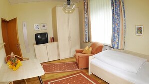Ein kleines Hotelzimmer mit Bett, Tisch, Stuhl, Kleiderschrank und Fernseher.