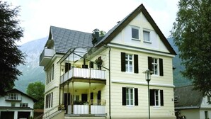 Ein zweistöckiges Gebäude mit einem Balkon im oberen Geschoss, einer Garage im Hintergrund und einem Berg in der Ferne.