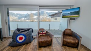 Una habitación moderna con un ventanal grande, televisor, sillones de cuero y un sillón informal.