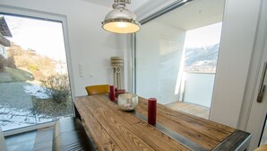 Un comedor moderno con una mesa de madera, velas rojas y vistas a las montañas a través de amplias ventanas.