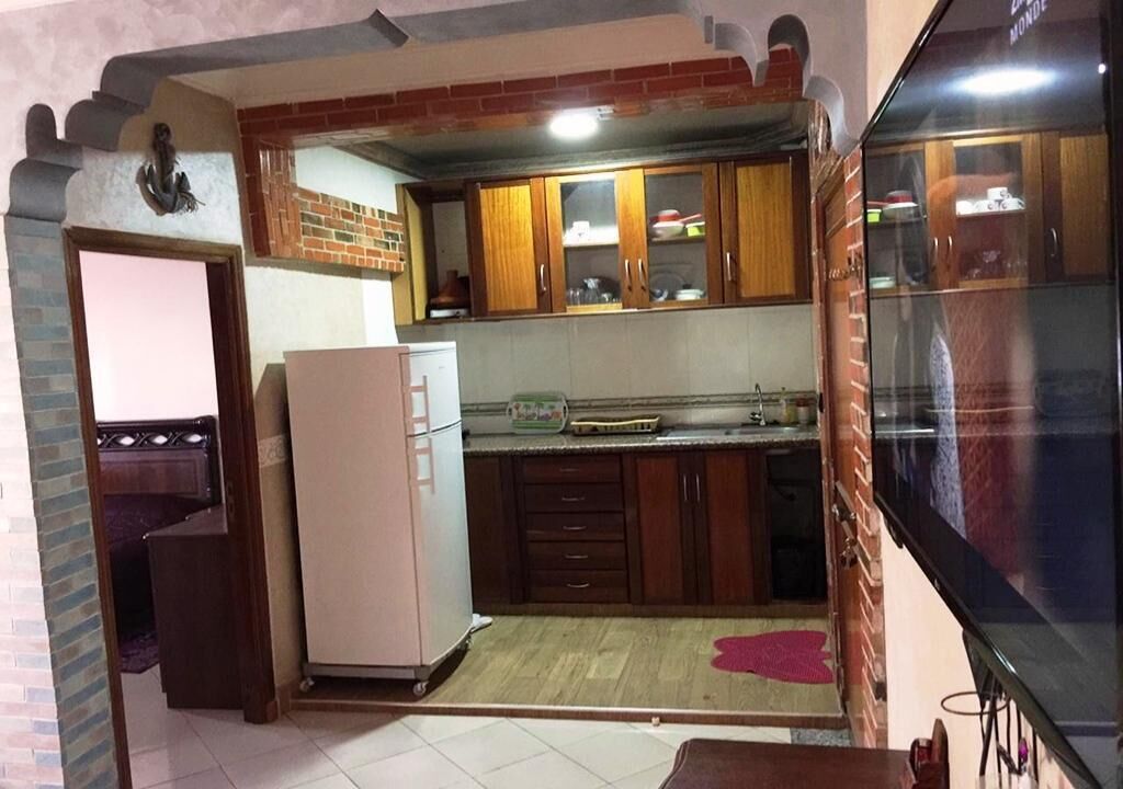 Eine kleine Küche mit Holzschränken, einem Kühlschrank und einem gefliesten Boden.