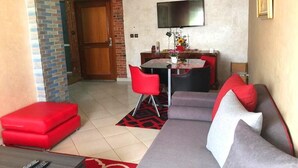 Una sala de estar con sofá, reposapiés rojo y un comedor con mesa y sillas.