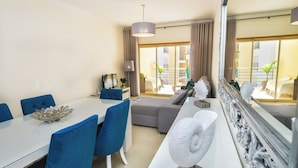 Quarto de hotel moderno com área de refeições, sofá, um espelho grande e vista para a varanda externa.