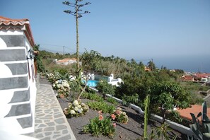 Un quartier résidentiel avec un sentier en pierre, des parterres de fleurs et une vue sur la mer.