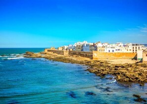 A coastal town with buildings along the shoreline, a clear blue sky, and calm sea. - Nice apartment in Essaouira 4159 (Essaouira)