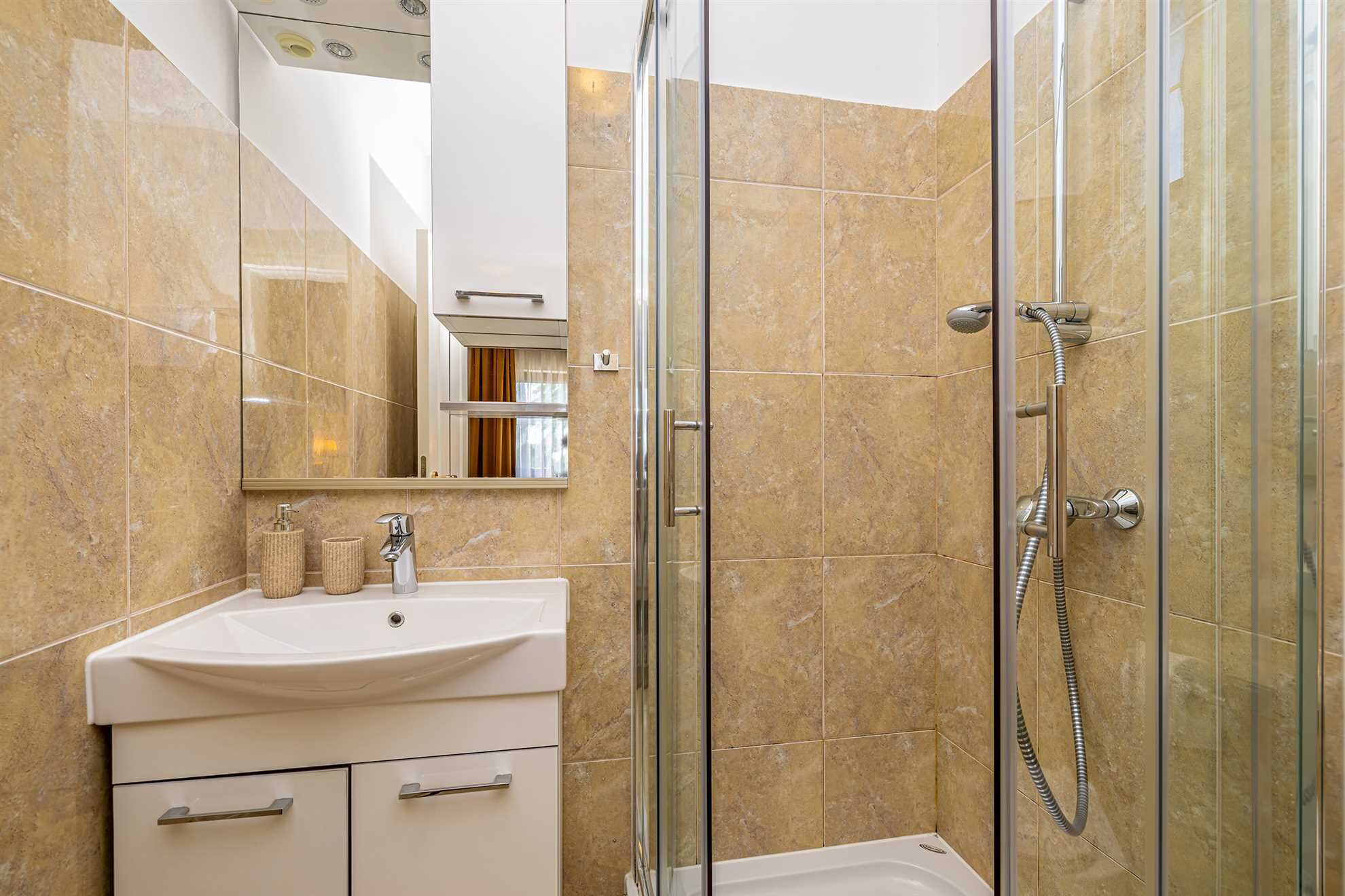 Une salle de bain moderne avec une douche à parois de verre, un lavabo blanc et un miroir au-dessus du lavabo.
