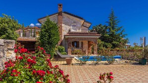 A villa with a stone facade, a swimming pool, and a garden with red flowers. - Luxury villa RUSTICA with private pool, jacuzzi and outdoor sauna (Linardići)