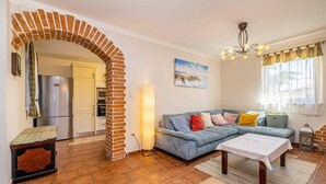A living room with a blue sofa, a wooden coffee table, a brick archway, a kitchen area with a refrigerator, and a painting on the wall. - Luxury villa RUSTICA with private pool, jacuzzi and outdoor sauna (Linardići)