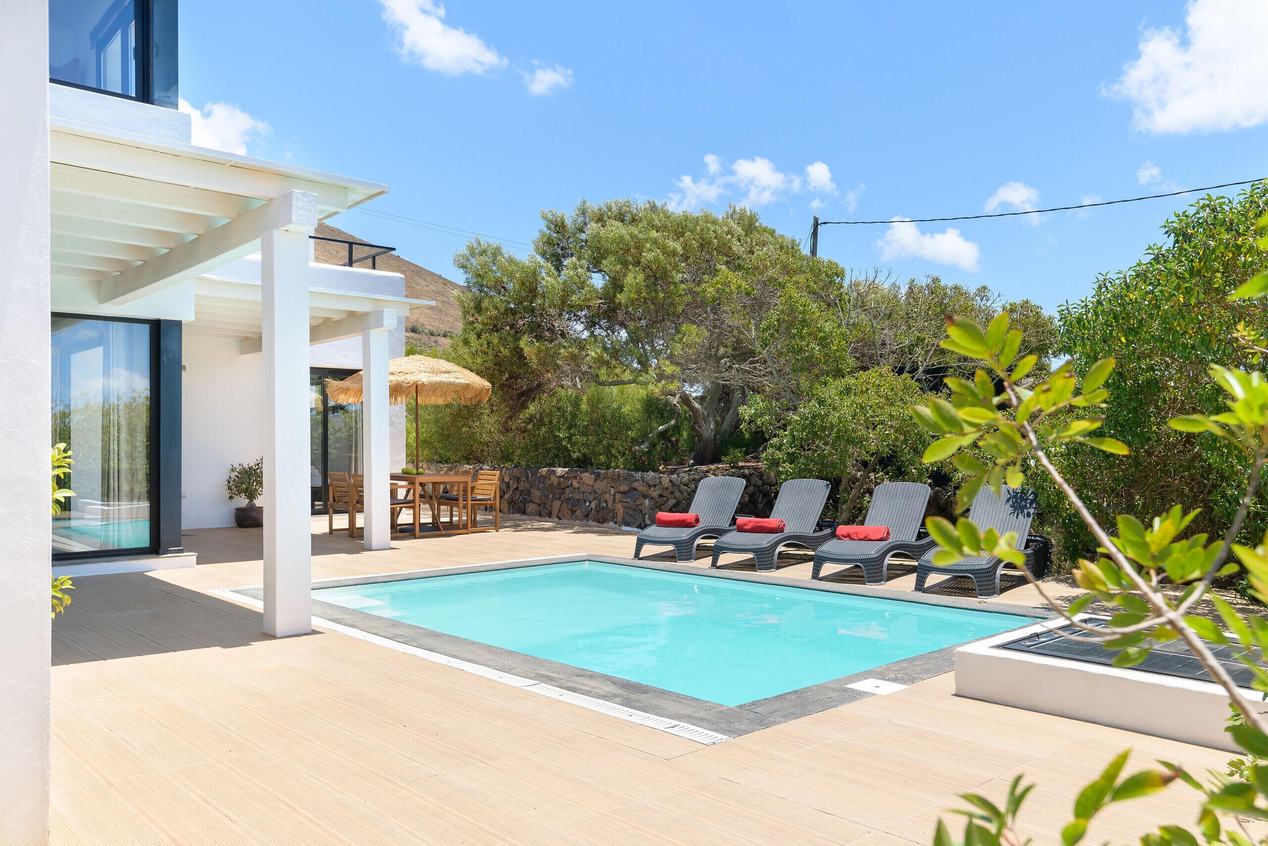 A modern outdoor pool area with a clear blue pool, lounge chairs, and a pergola.