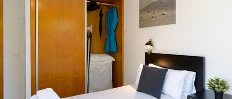 Ein Hotelzimmer mit Bett, Nachttisch mit Lampe, einem Bild an der Wand und einem Schrank mit Bademantel und Handtüchern.