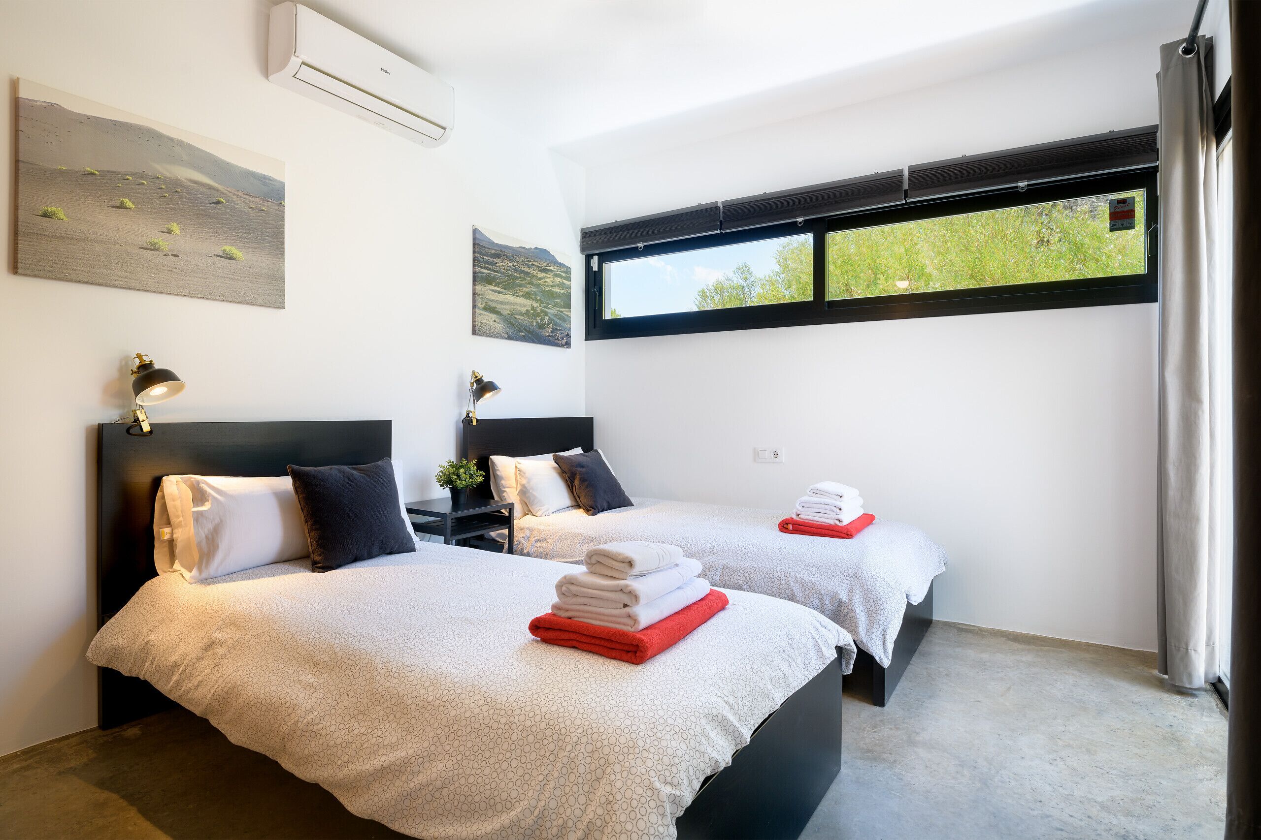 A hotel room with two beds, a large window with a view of greenery, and artwork on the walls.