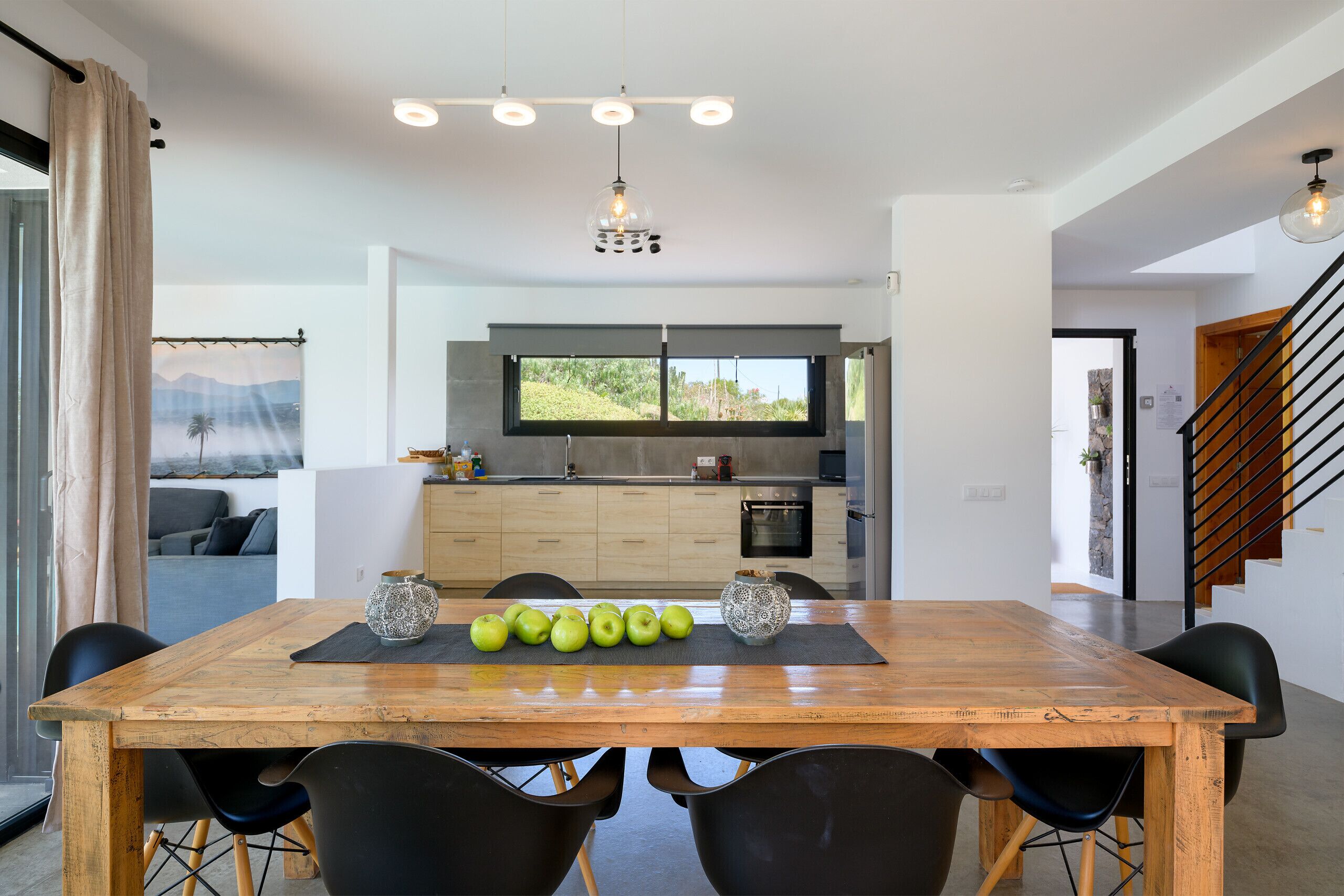 A modern dining area with a wooden table, black chairs, and a view of the kitchen and living area.
