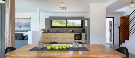 A modern dining area with a wooden table, black chairs, and a view of the kitchen and living area.