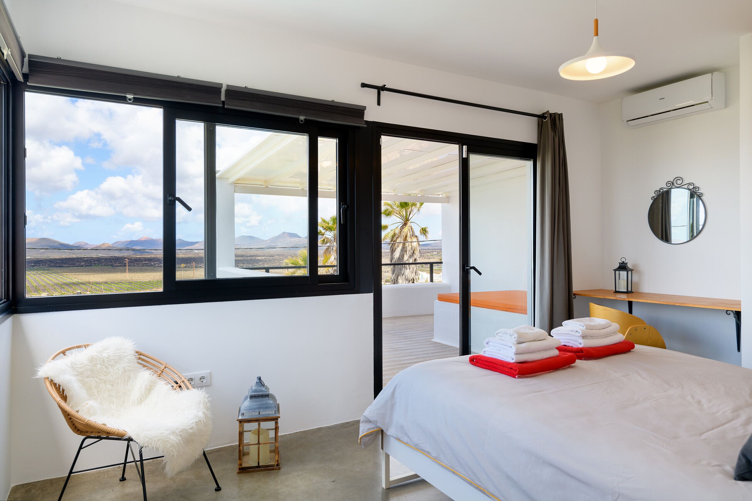 Ein Schlafzimmer mit großem Fenster, einem Bett mit ordentlich gefalteten Handtüchern, einem Korbstuhl und einer kleinen Laterne.