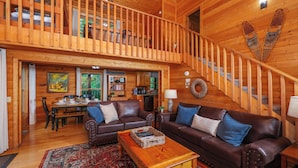 A spacious wooden cabin with a dining area, a living room with leather sofas, and a staircase. - Very Private with Incredible Mountain Views! Free Pool and Putt Putt Access! (Sevierville)