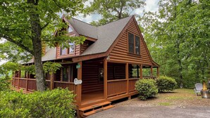 A wooden cabin with a porch, surrounded by trees and a fire pit. - Very Private with Incredible Mountain Views! Free Pool and Putt Putt Access! (Sevierville)